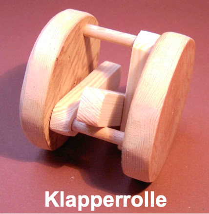 Holzspielzeug mit zwei runden Scheiben und einem Würfel in der Mitte, auf einem braunen Hintergrund. Text "Klapperrolle" darunter.